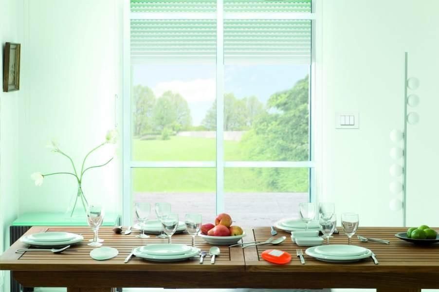 Tavolo da pranzo apparecchiato per un pasto davanti a una finestra con vista su un prato verde e sugli alberi.