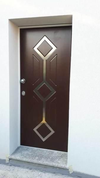 Porta marrone con dettagli a forma di diamante e geometrici in argento, inserita in una parete bianca.