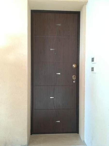 Porta marrone con telaio scuro e ferramenta argentata inserita in un ingresso bianco.