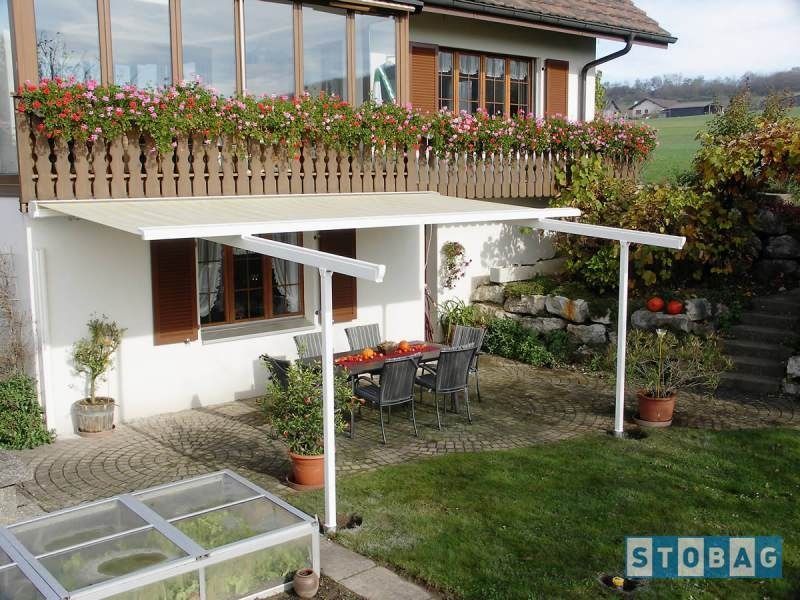 Una tenda da sole beige ombreggia un patio con tavolo e sedie accanto a una casa con una fioriera.