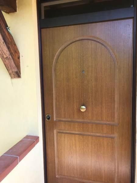 Porta in legno con pannello superiore arcuato e pomolo dorato, incastonata in una cornice.