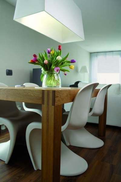 Tavolo da pranzo con vaso di tulipani colorati, sedie bianche moderne e lampada a sospensione rettangolare.