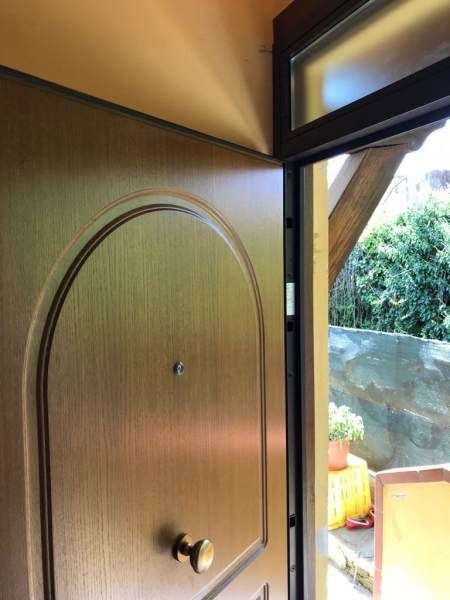 Porta di legno, leggermente aperta, che lascia intravedere l'esterno; stipite marrone, parete beige.