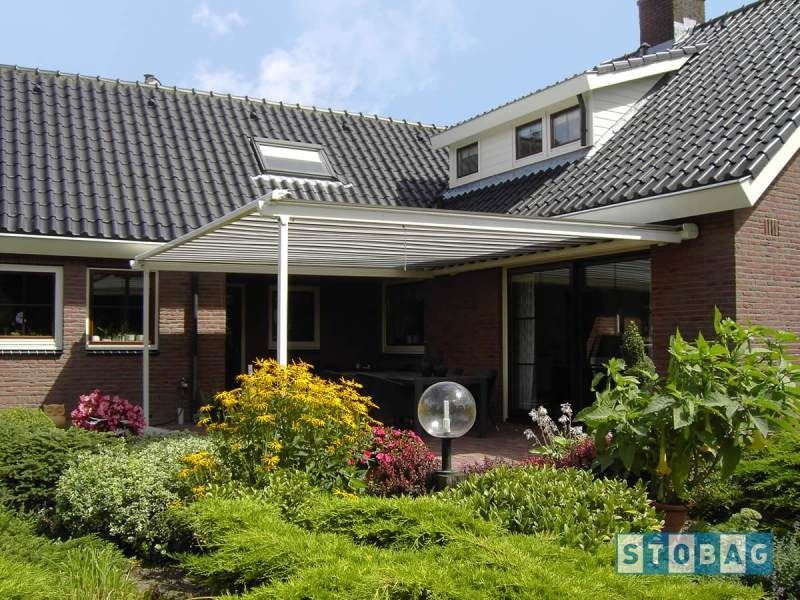 Patio sul retro con tenda da sole bianca, piante e una casa in mattoni.