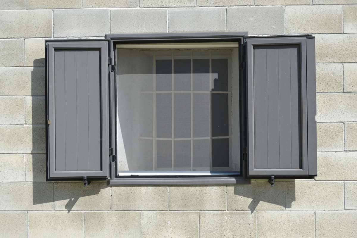 Finestra con persiane grigie aperta su un muro di blocchi di cemento.