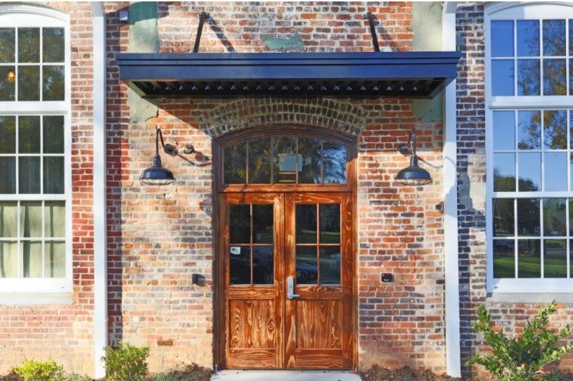 Exterior entrance with wooden double doors and brick wall. At Waxhaw Mills, our apartments for rent in Waxhaw, NC offer the best in service and enviable amenities. Experience all our community has to offer. Contact us to set up a tour!