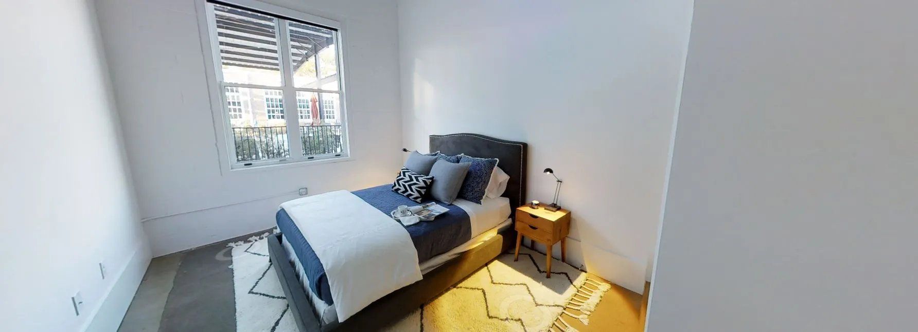 Modern bedroom with a bed, bedside table, and window. Contact us to learn more about our pet-friendly apartments in Waxhaw, NC, and make Waxhaw Mills your home today!