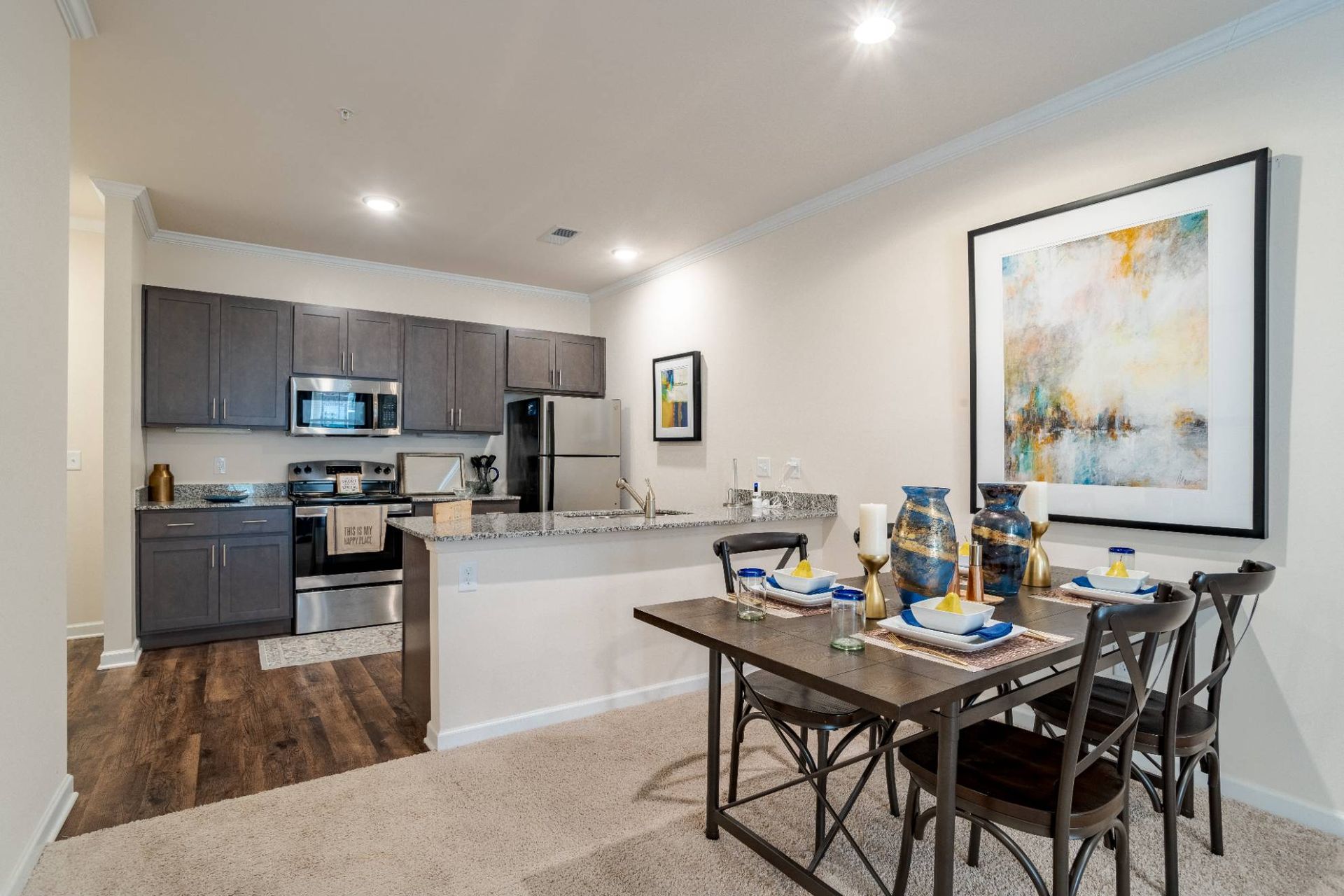 Open-concept kitchen and dining area with grey cabinets and granite countertops. Contact us to learn more about our pet-friendly apartments in Waxhaw, NC, and make Waxhaw Mills your home today!