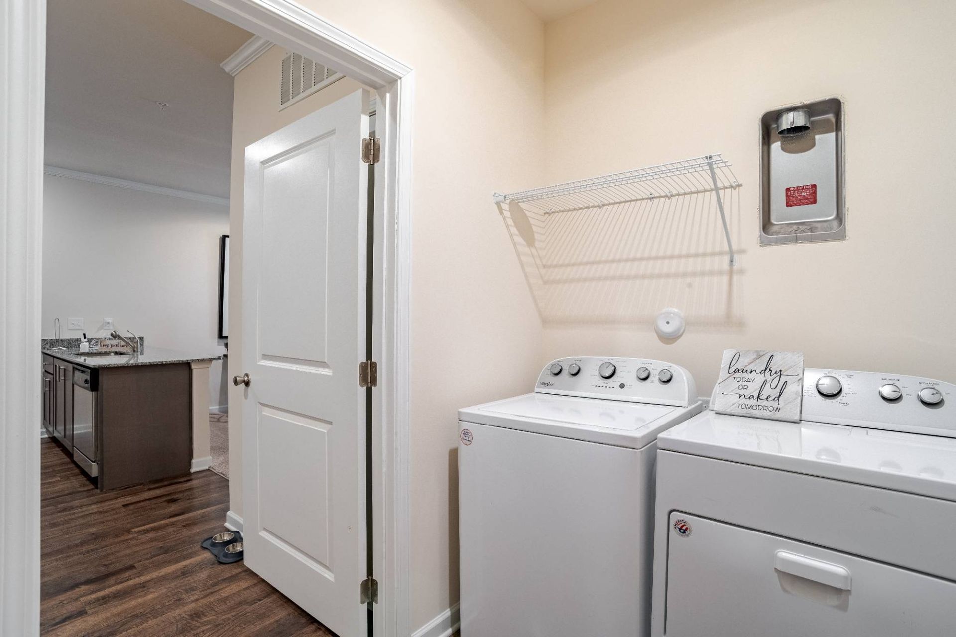 Laundry room with side-by-side washer and dryer and a wire shelf. Contact us to learn more about our pet-friendly apartments in Waxhaw, NC, and make Waxhaw Mills your home today!
