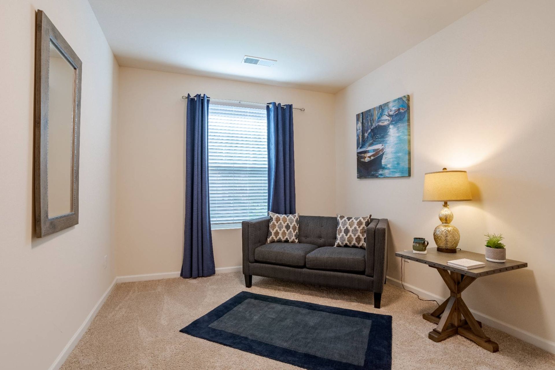 Cozy living room with gray sofa, blue curtains, wall art, and a side table lamp. Contact us to learn more about our pet-friendly apartments in Waxhaw, NC, and make Waxhaw Mills your home today!