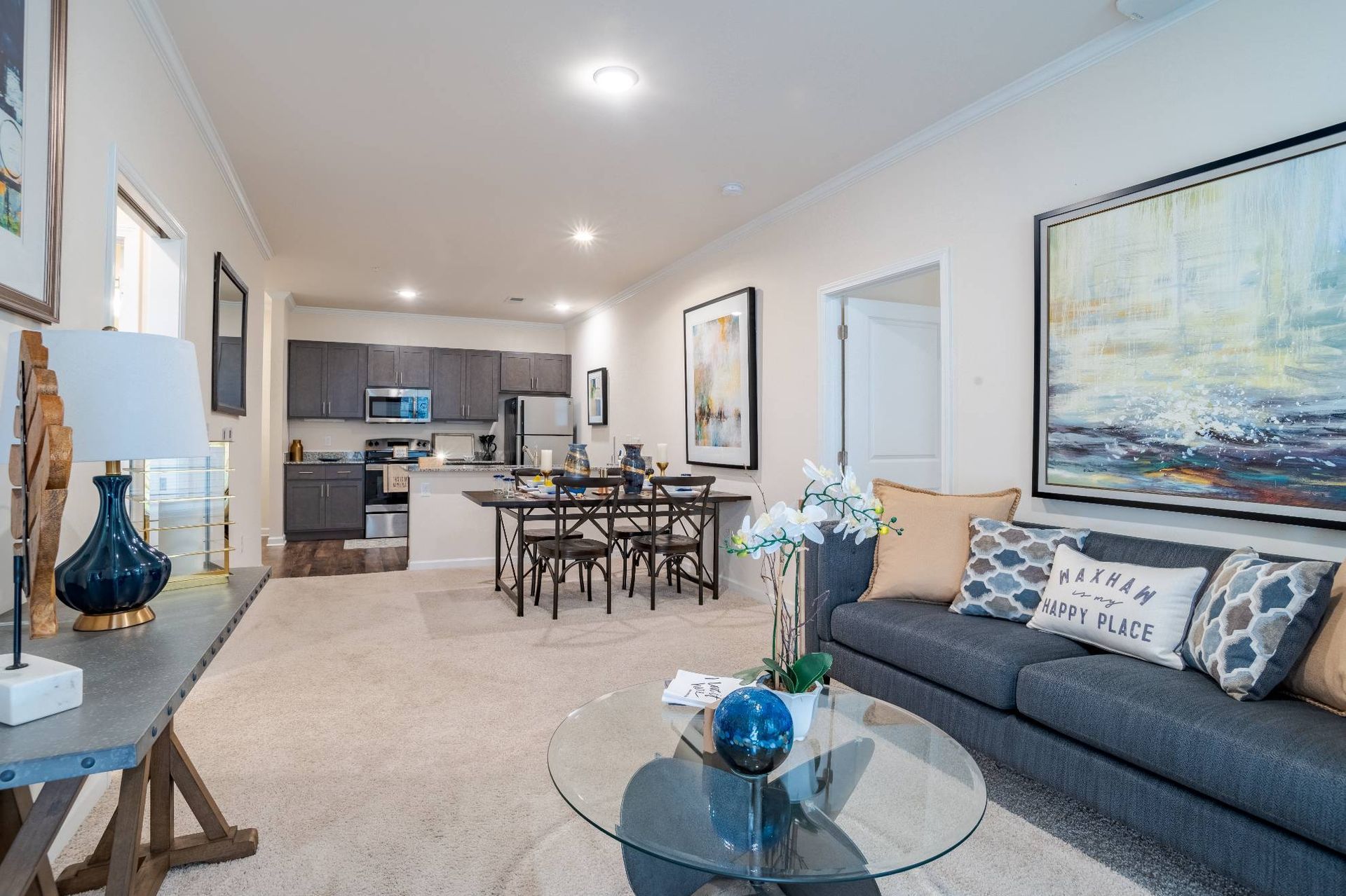 Open-concept living room with sofa, glass coffee table, and visible kitchen. Interested in learning more about our 1, 2, and 3-bedroom apartments in Waxhaw, NC? Contact us today to schedule your tour!