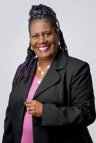 Woman with purple hair and patterned dress, smiling.