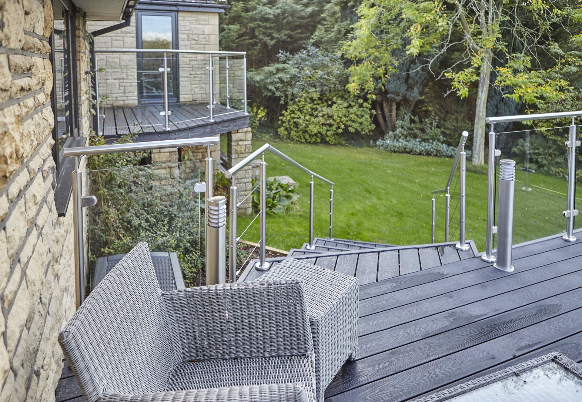 A wicker chair is sitting on a deck next to a staircase leading to a lush green yard.
