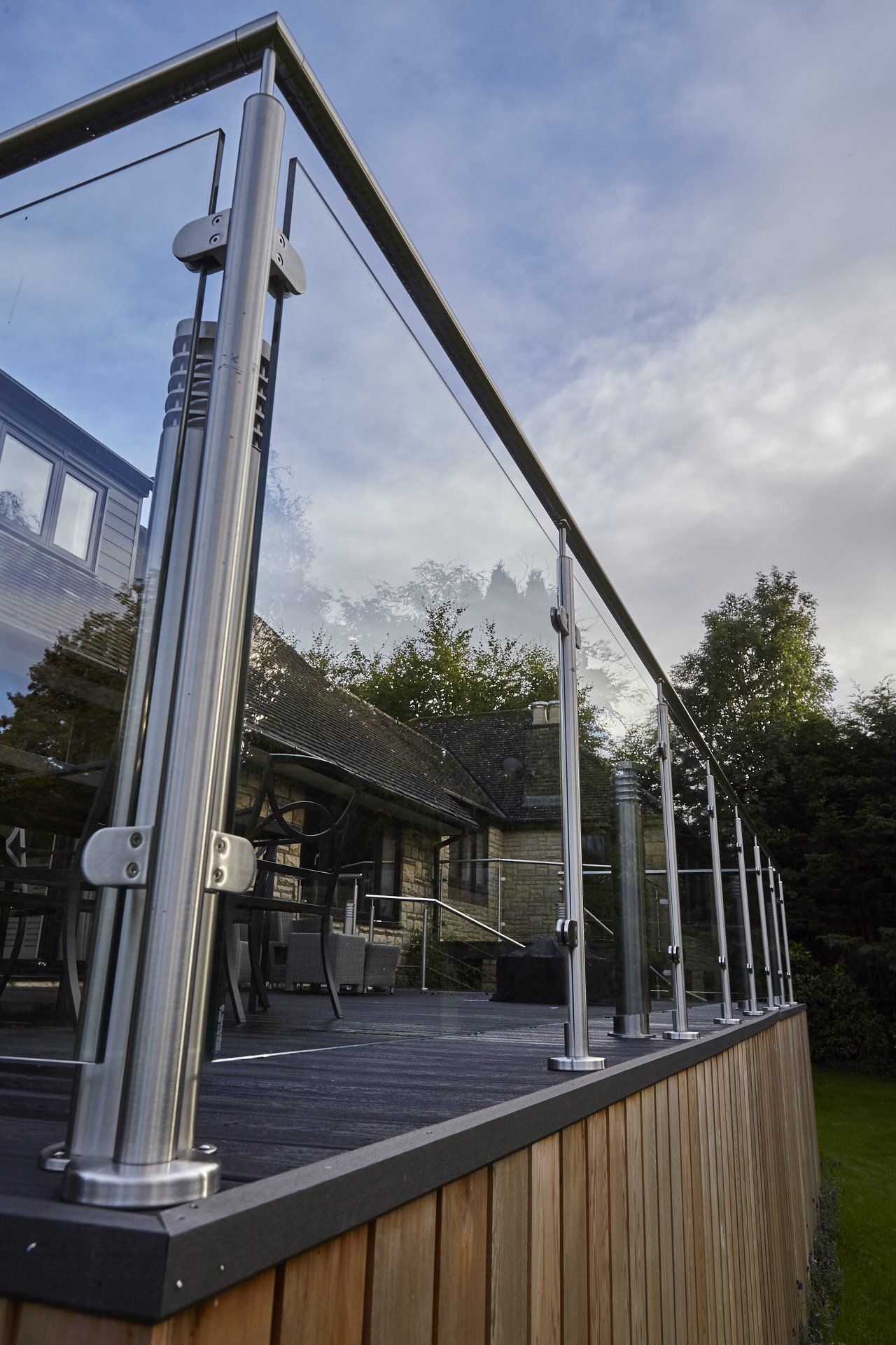 A wooden deck with a glass railing and a house in the background.