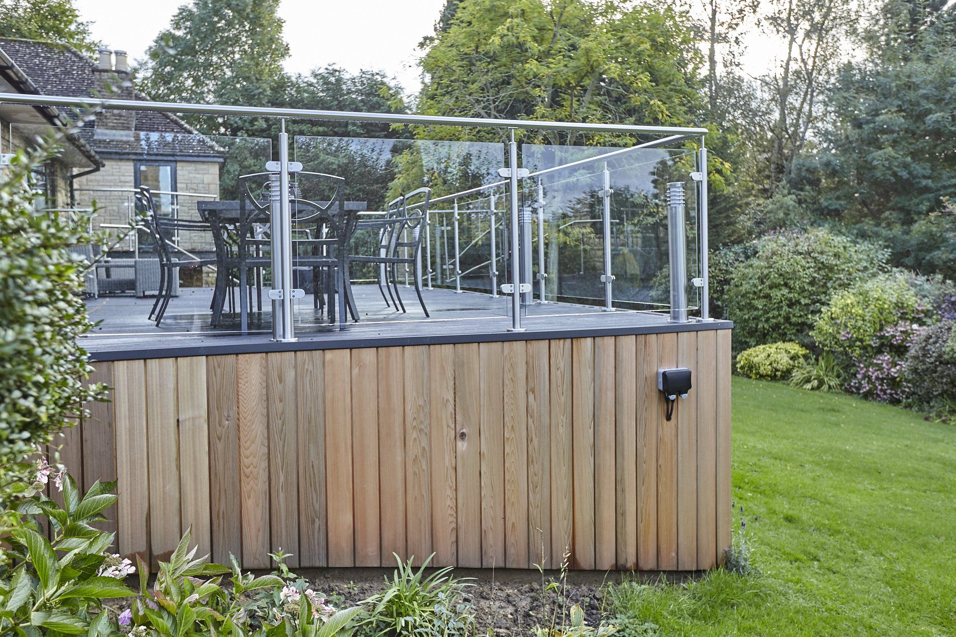 A wooden deck with a glass railing in the backyard of a house.