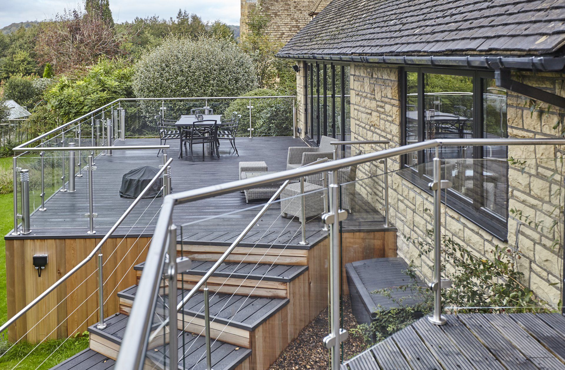 A wooden deck with stairs leading up to it and a stainless steel railing.
