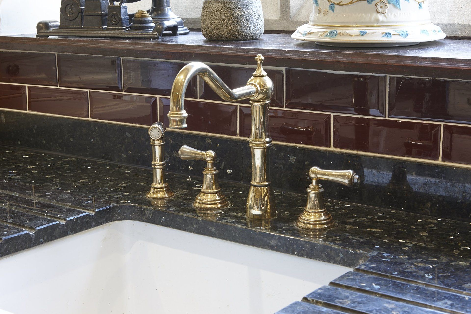 A kitchen sink with a brass faucet and black counter top