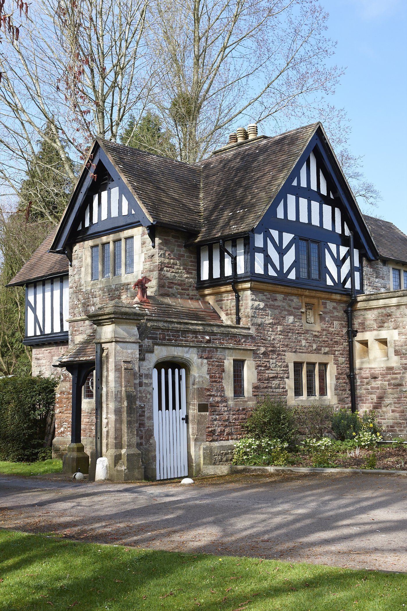 A large brick house with a black and white trim is sitting on top of a lush green hillside.