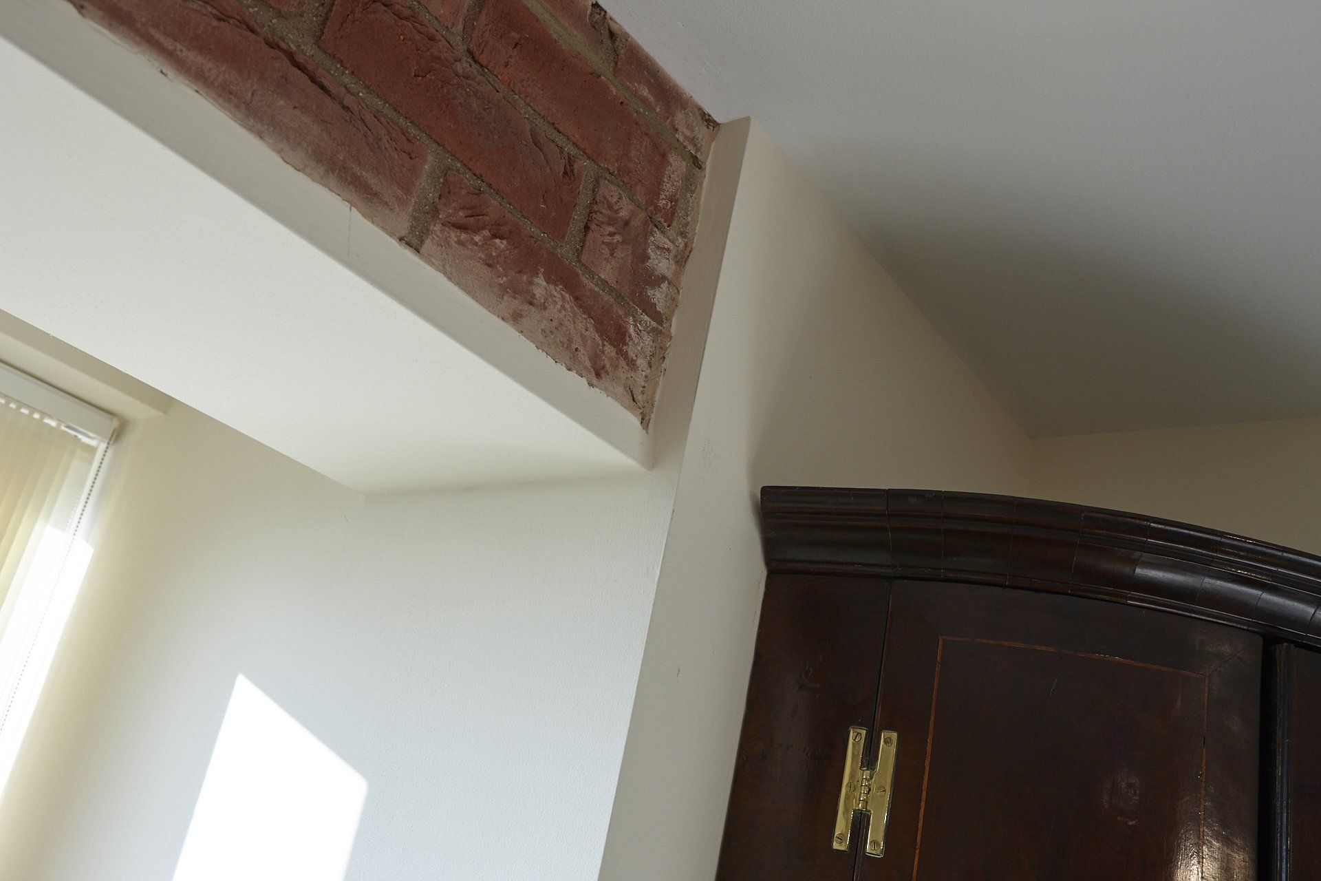 A corner of a room with a brick wall and a wooden cabinet.