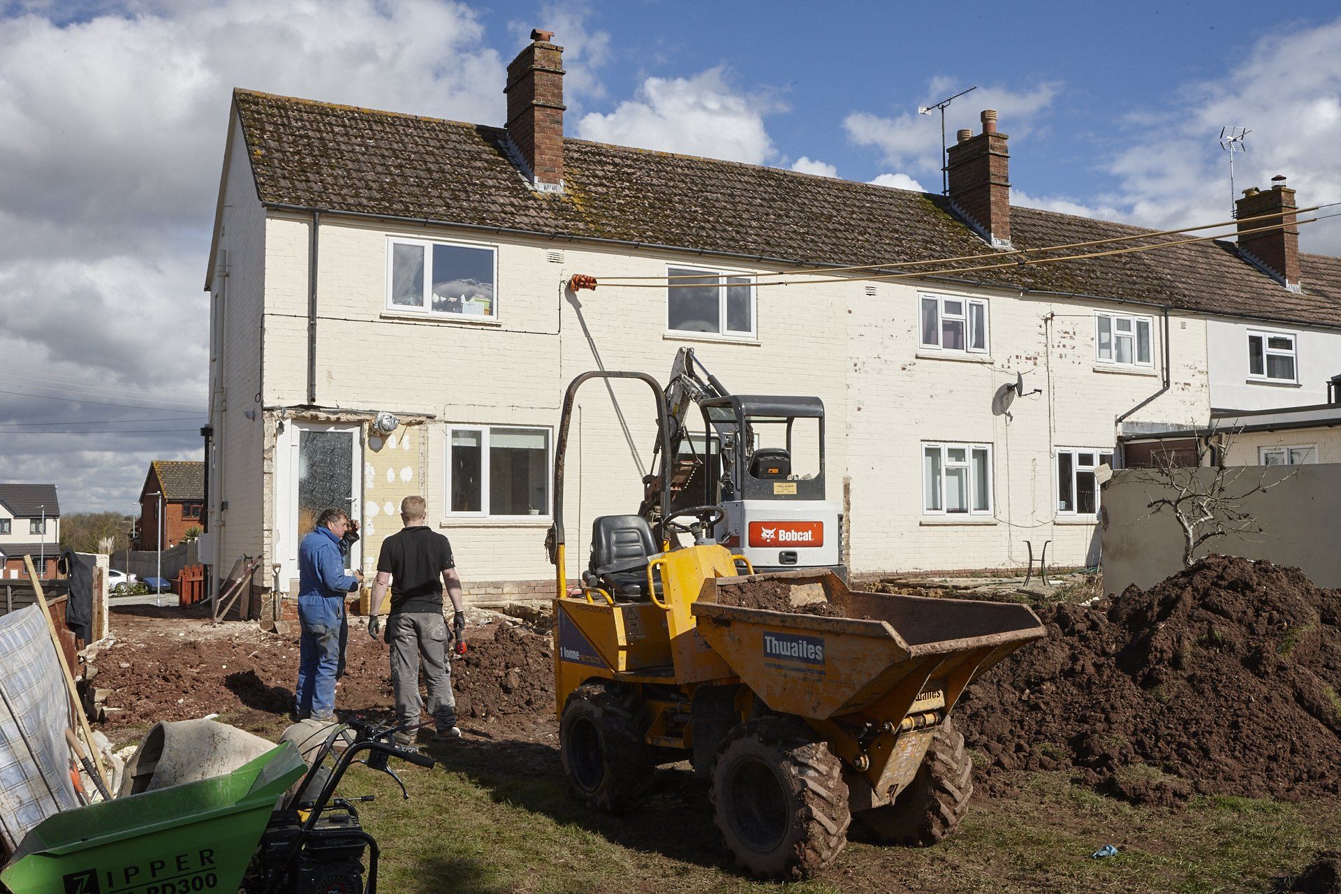 A bobcat dump truck is parked in front of a white house