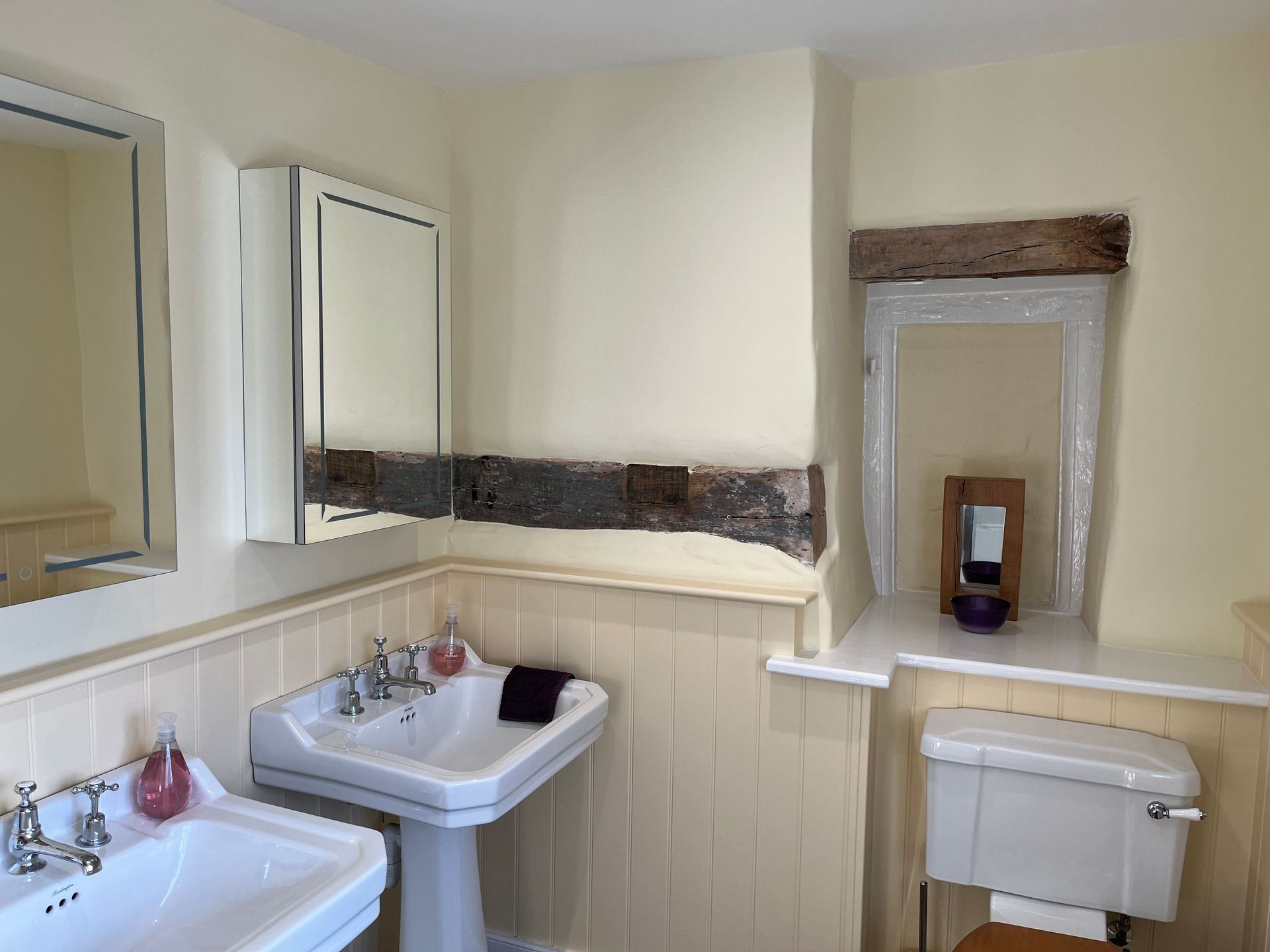 A bathroom with two sinks , a toilet and a mirror.