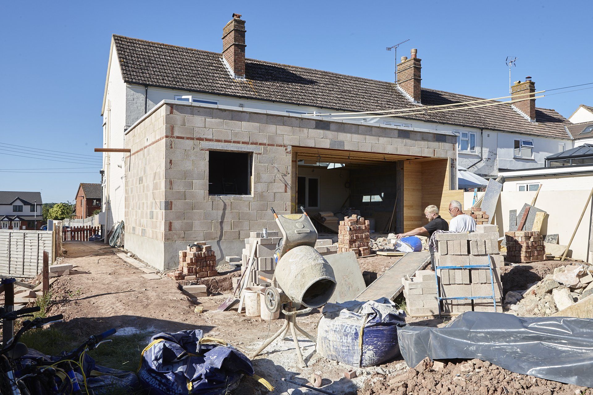 A house is being built with bricks and a cement mixer in front of it.
