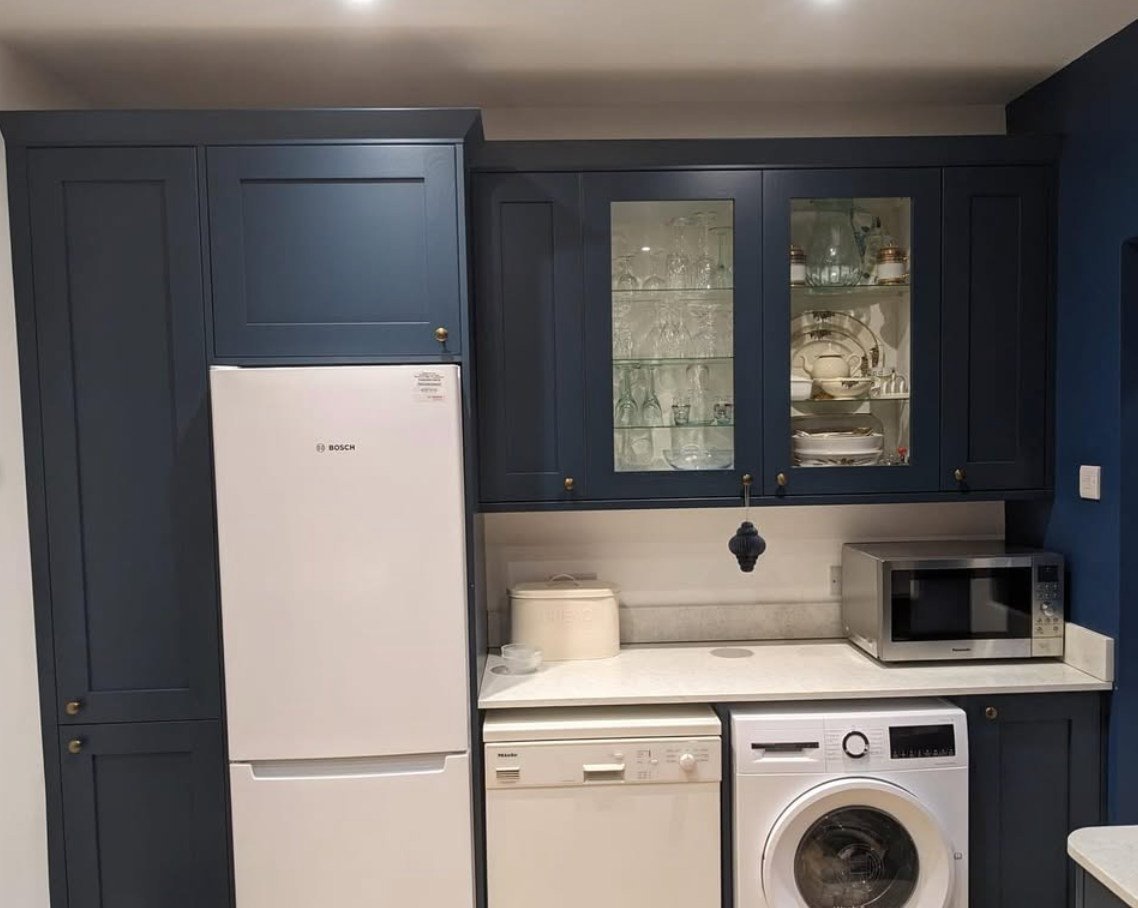 A kitchen with blue cabinets , a refrigerator , a washer and dryer , and a microwave.