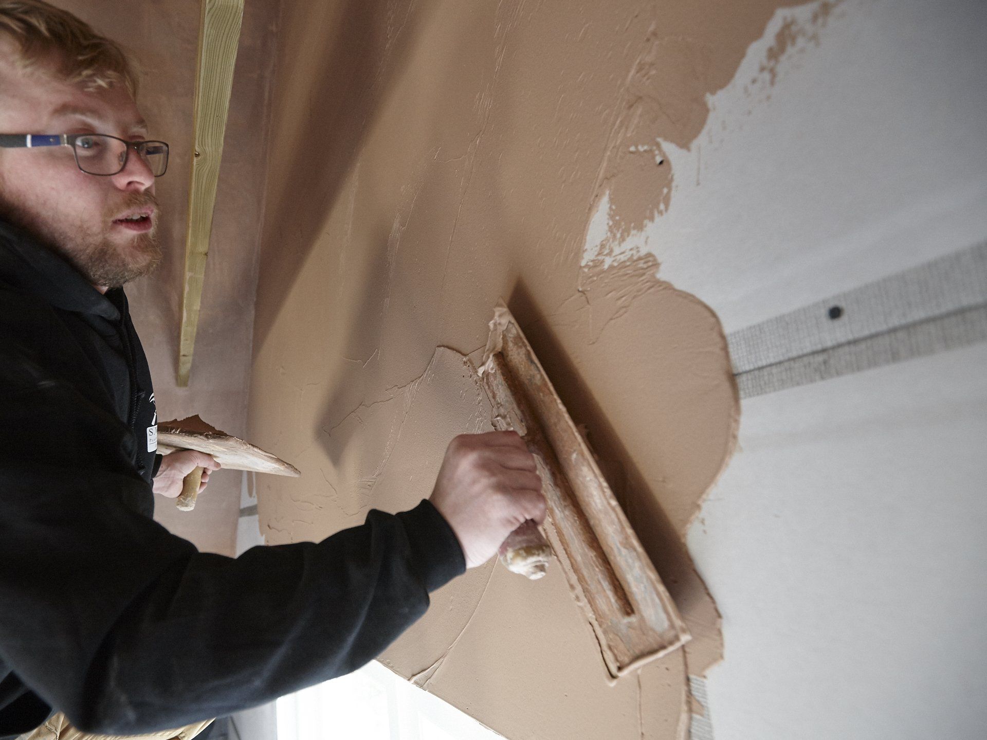 A man is plastering a wall with a trowel.