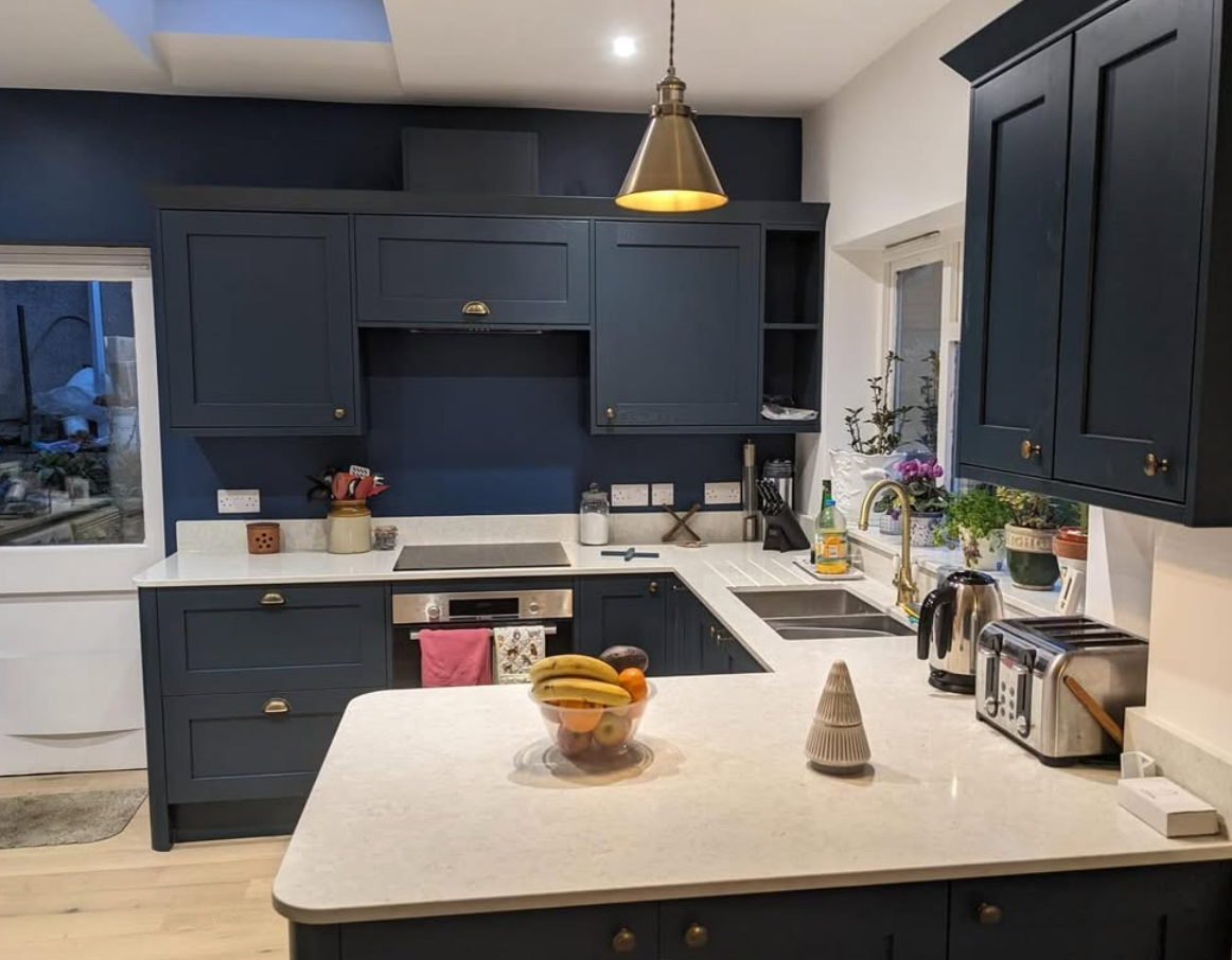 A kitchen with blue cabinets and white counter tops with a bowl of fruit on the counter.