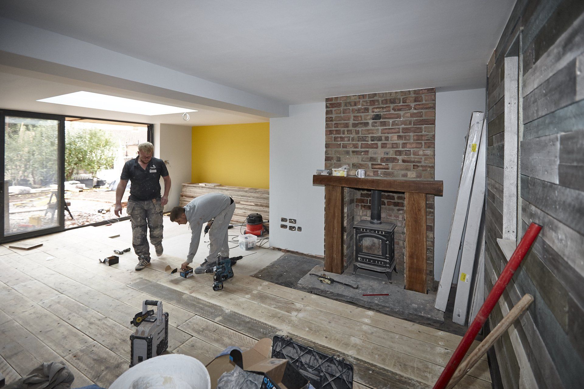 Two men are working on a fireplace in a living room.