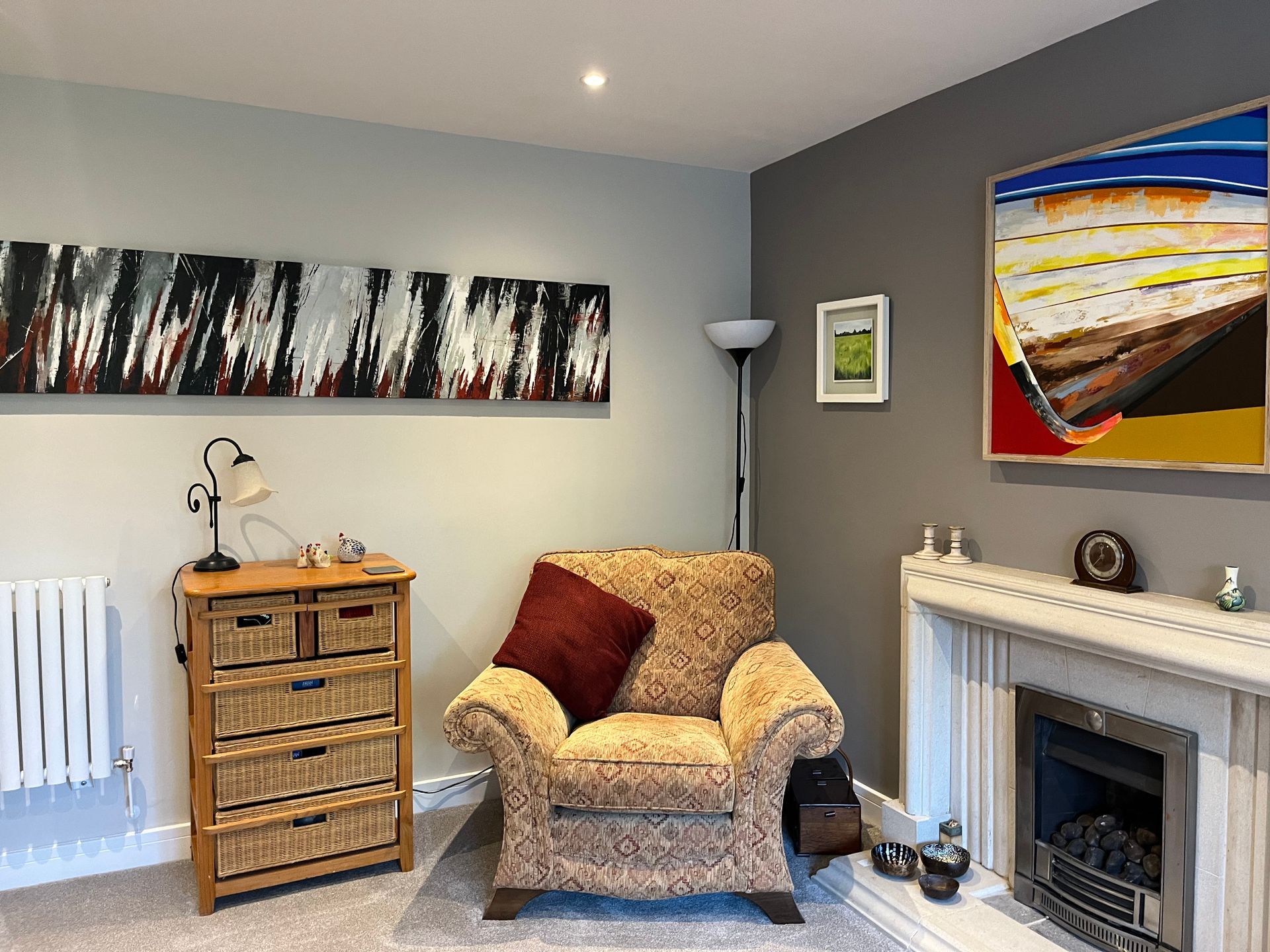 A living room with a fireplace , chair , dresser and painting on the wall.