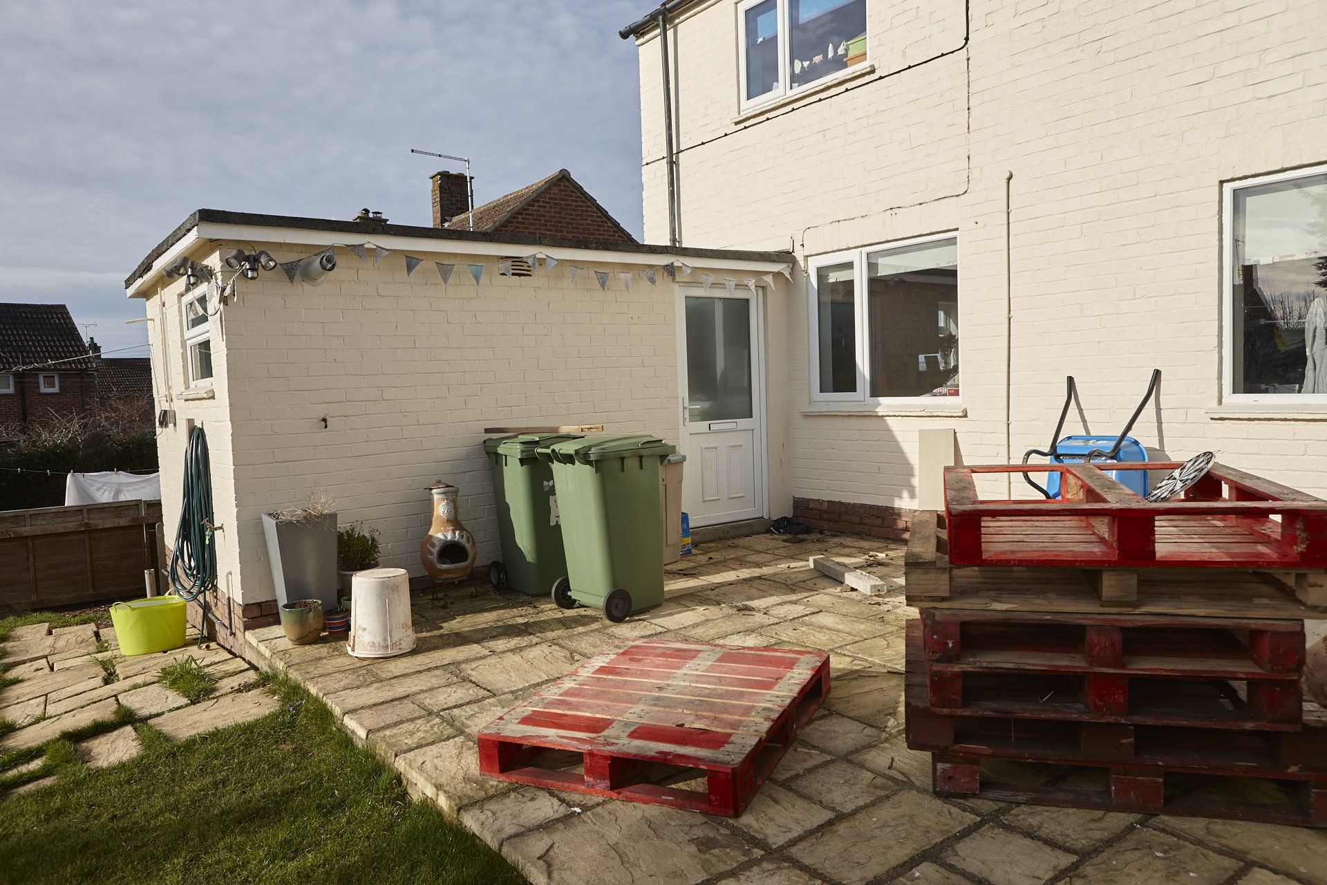 A patio with pallets and trash cans in front of a house