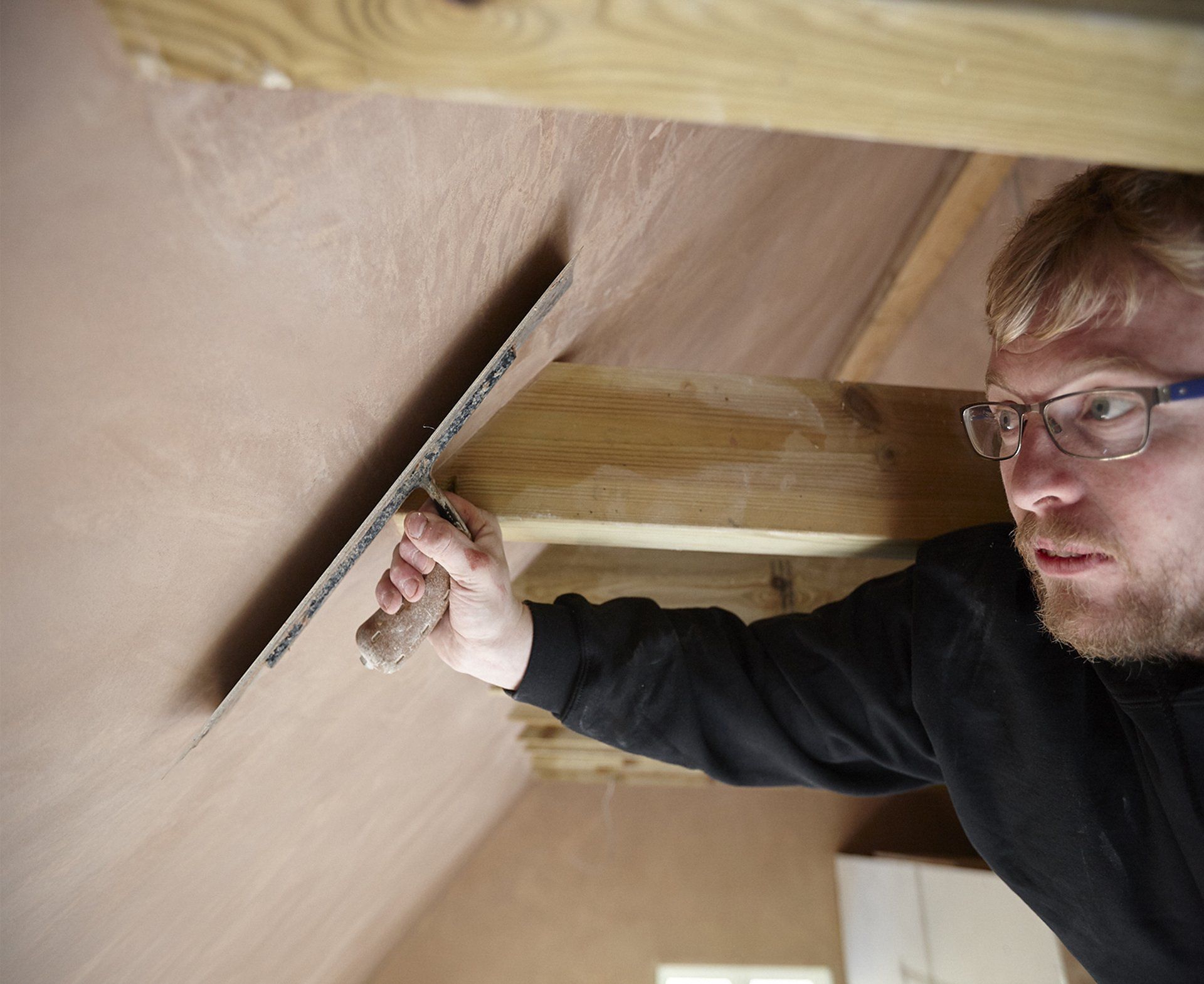 A man wearing glasses is using a trowel to plaster a wall