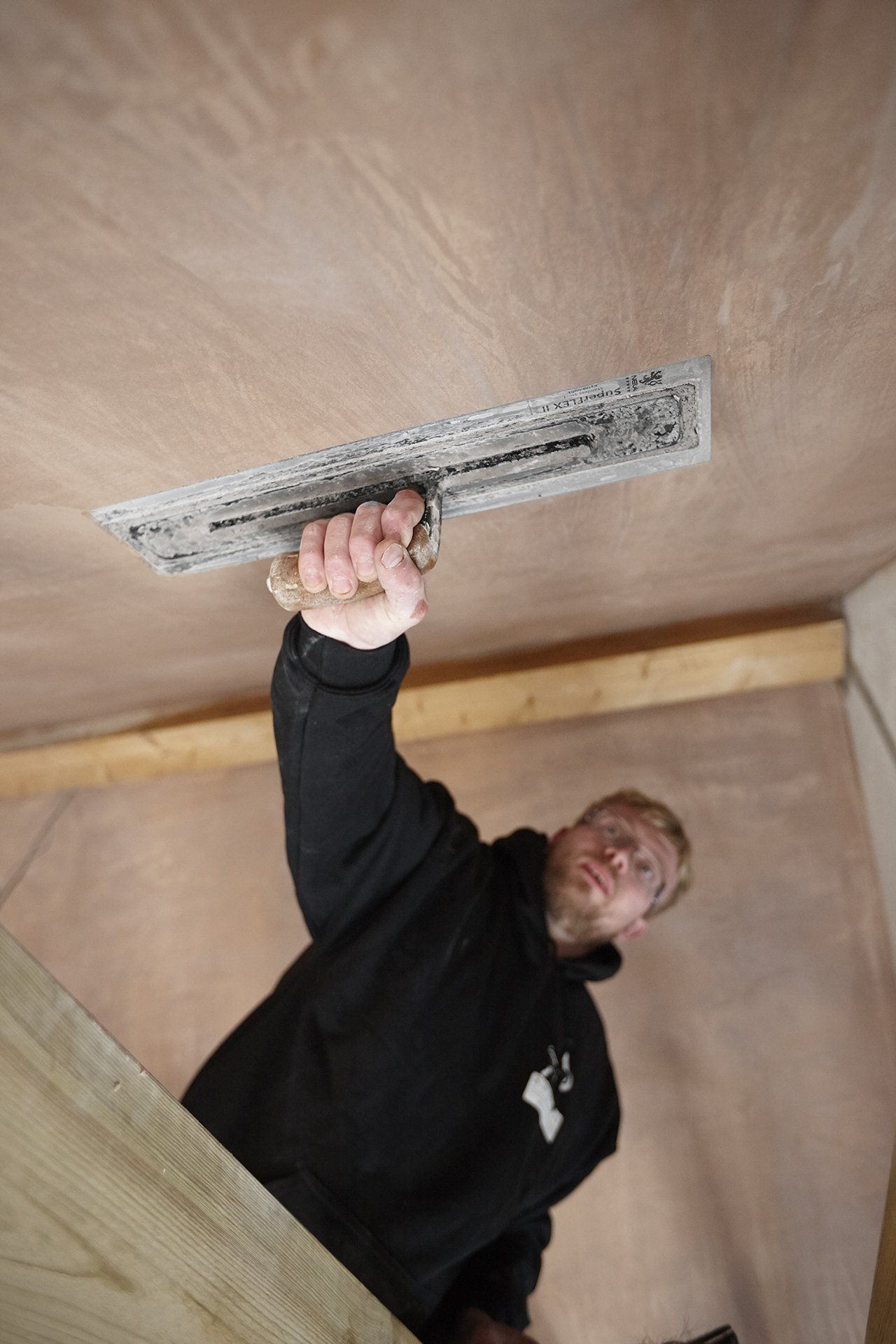 A man is using a trowel to plaster a ceiling.