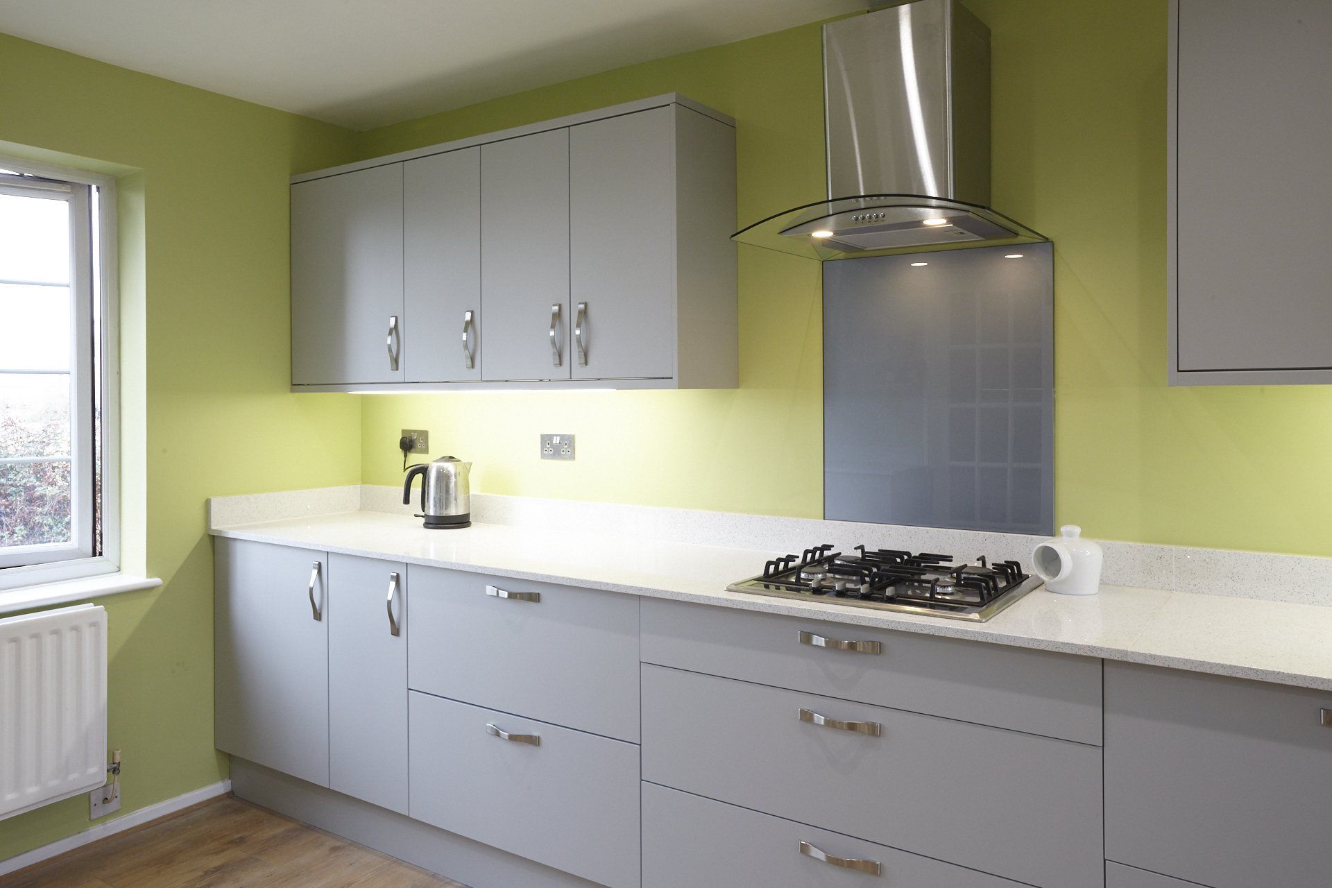 A kitchen with gray cabinets and green walls has a stove top oven.