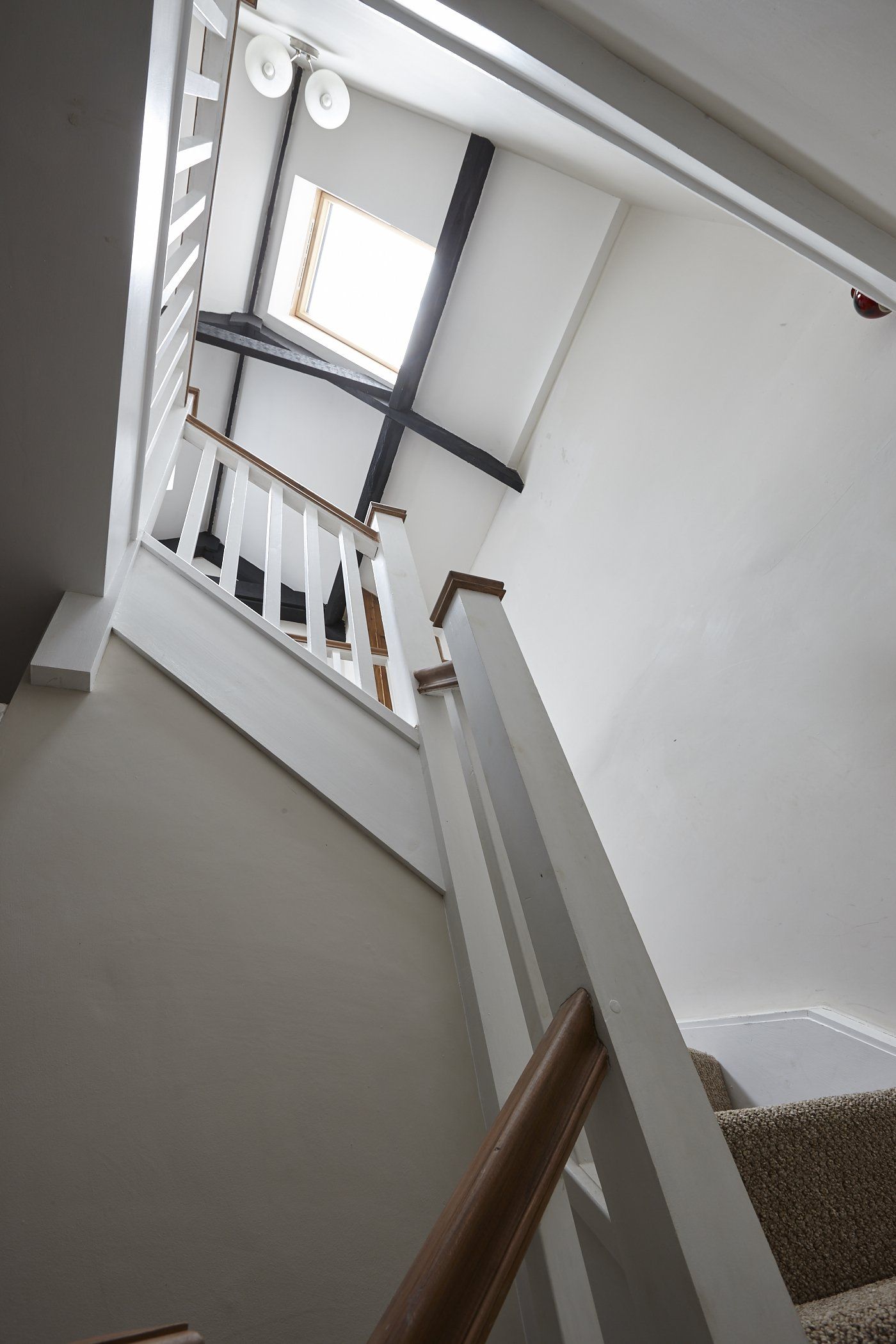 Looking up at a staircase with a wooden railing and a window.