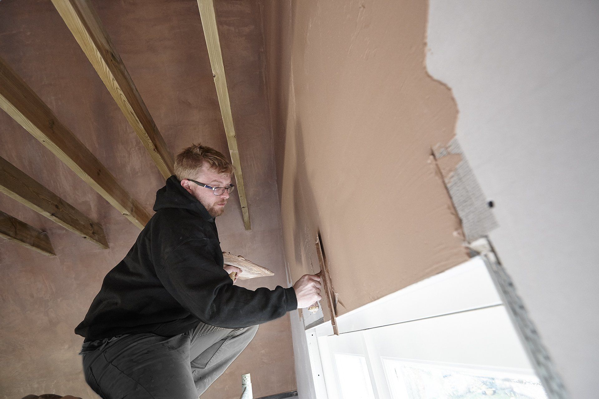 A man is kneeling down while working on a wall.
