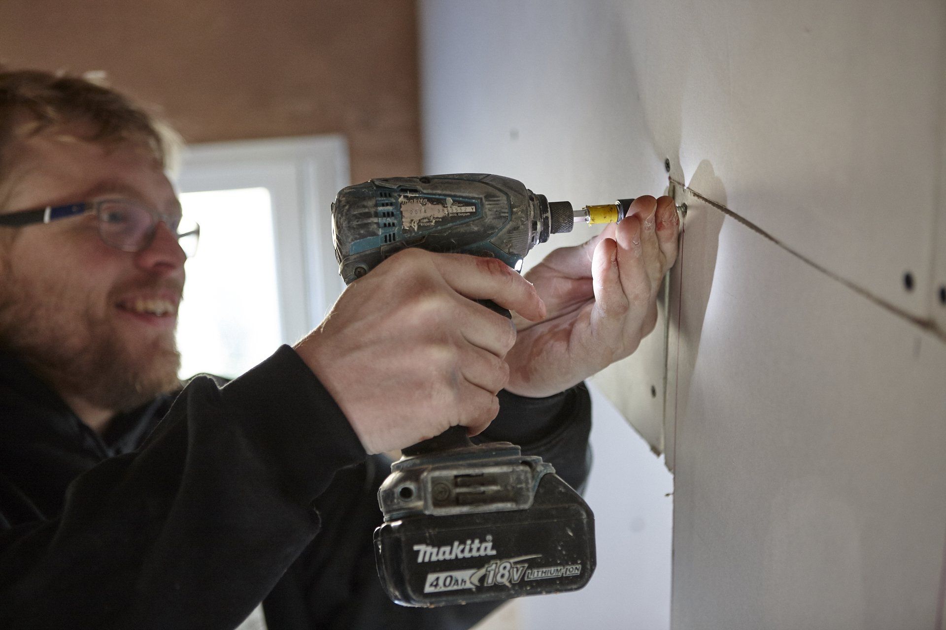 A man is using a makita cordless drill on a wall.