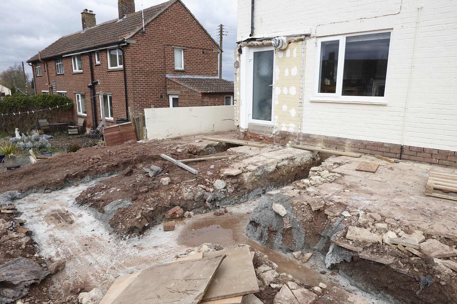 A brick house is being demolished and a white house is in the background.