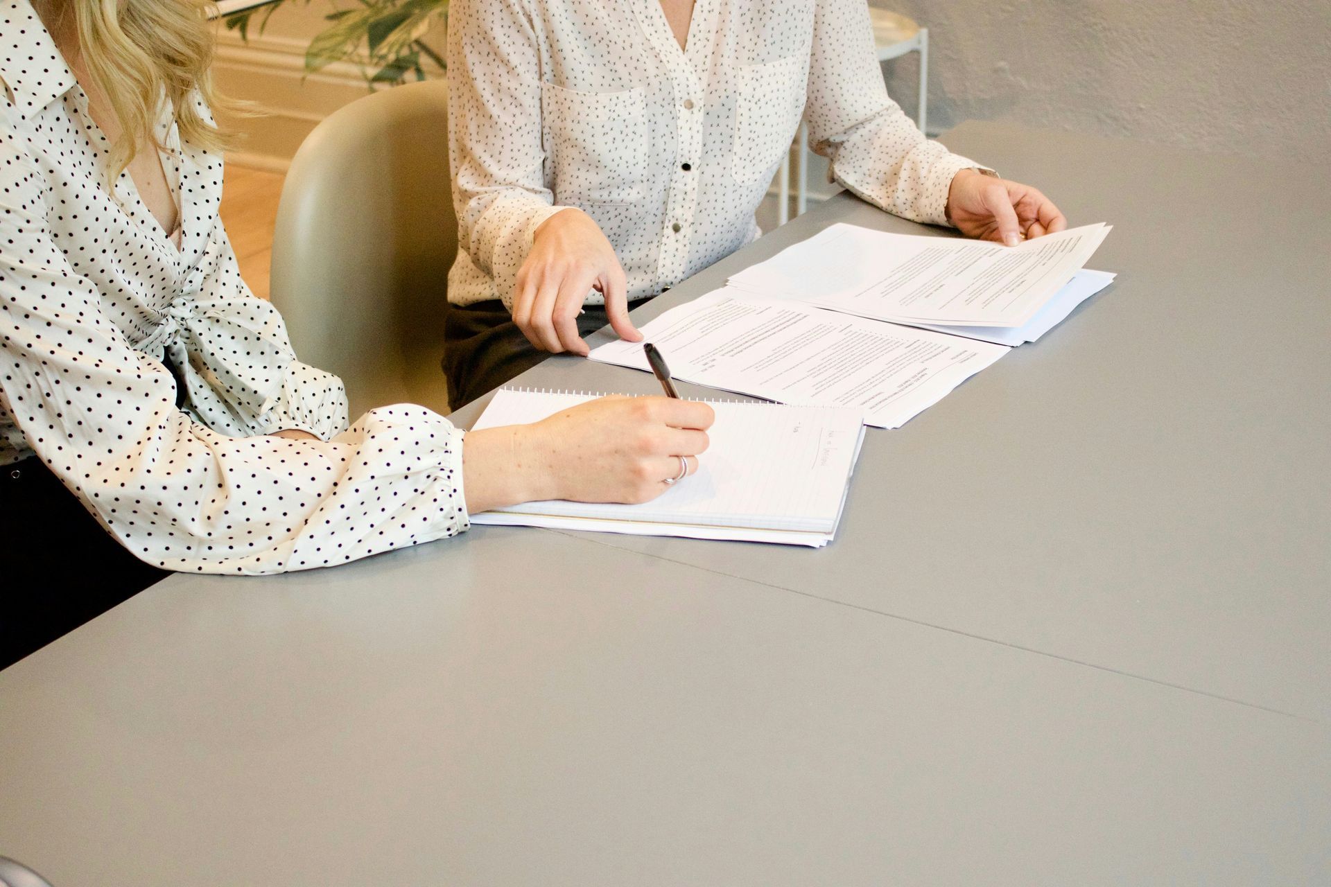 Two people at a table reviewing documents; one writes with a pen.