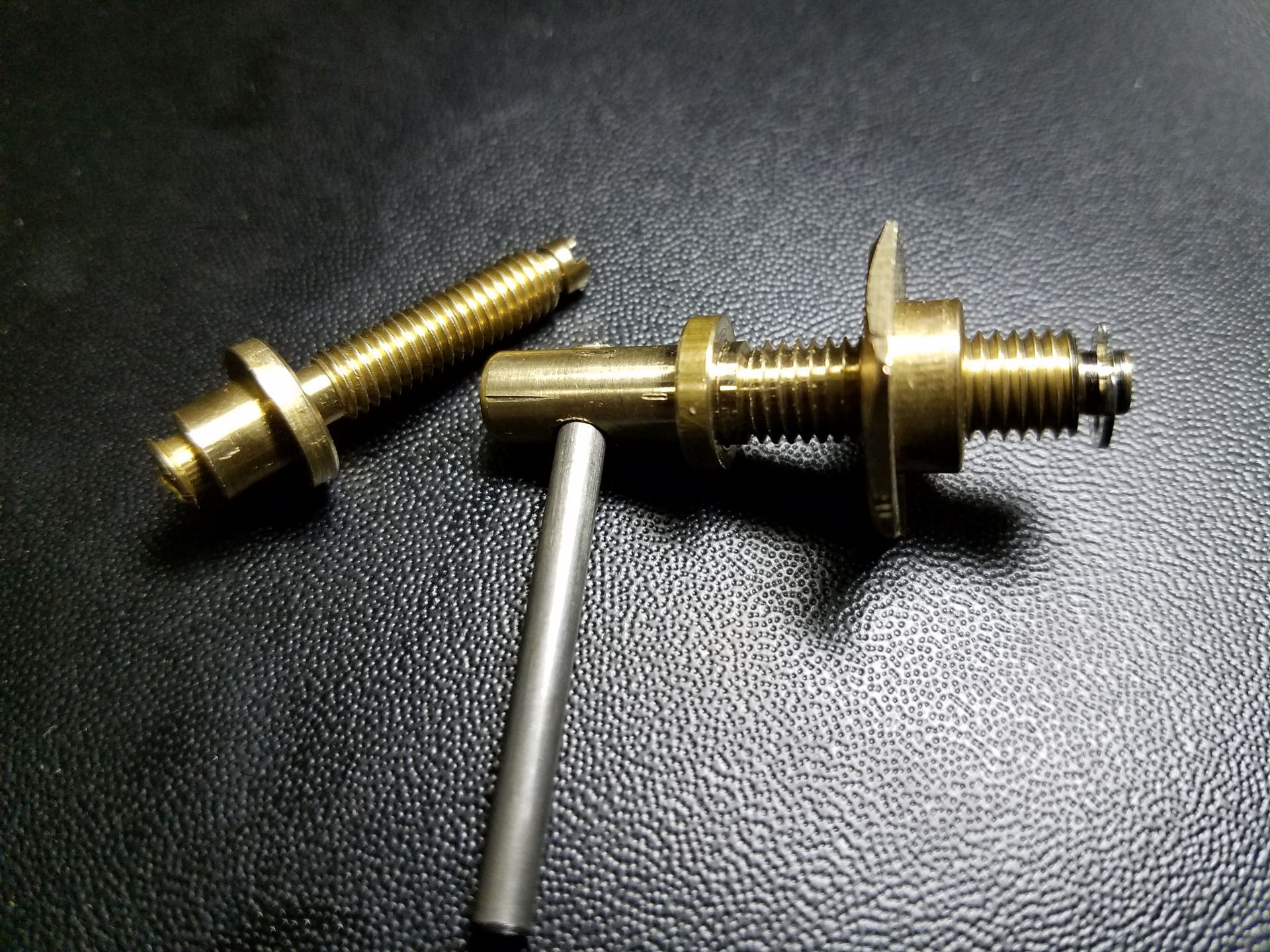 Brass screws and a metal pin on a black surface