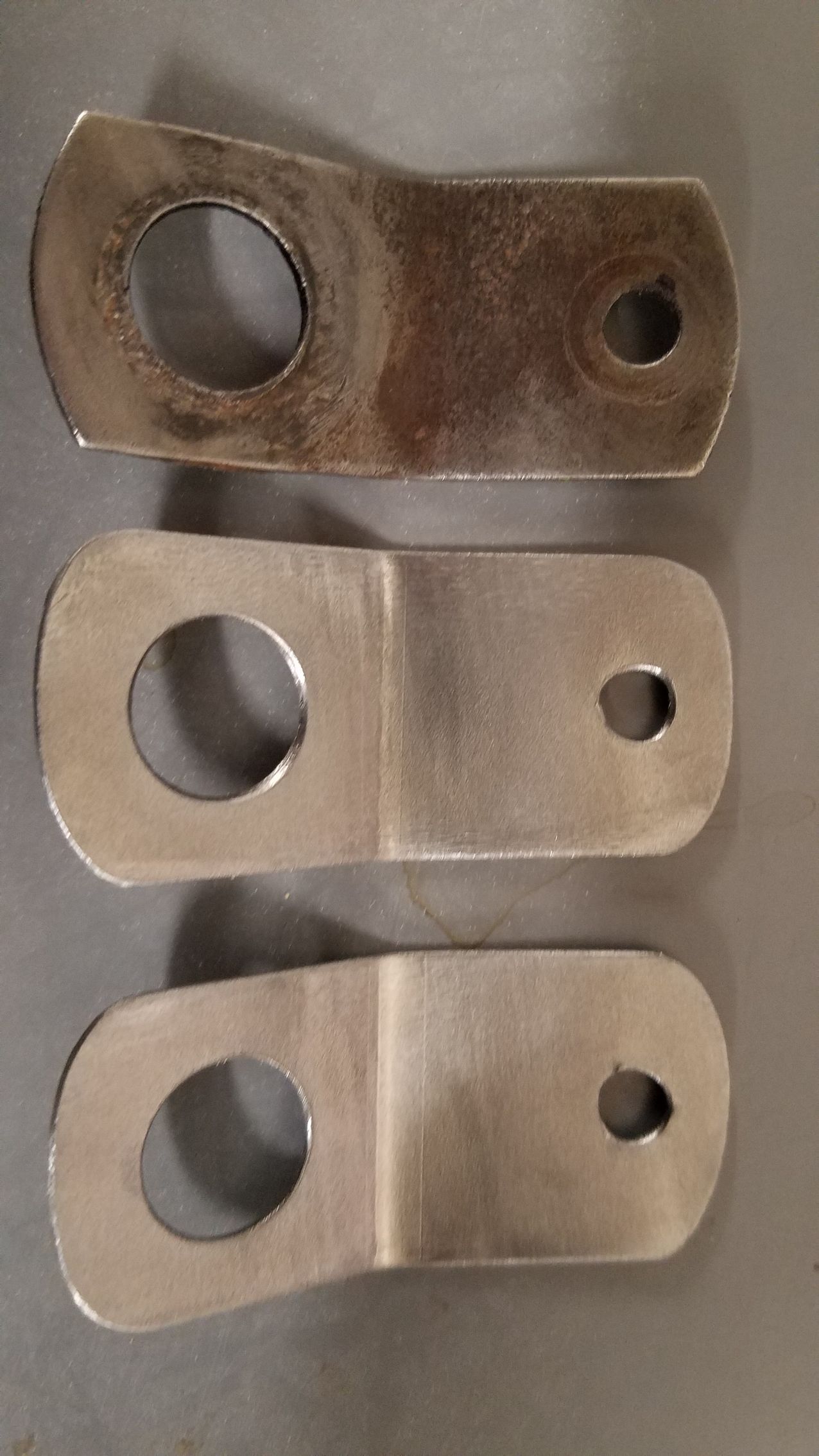 Three pieces of metal with holes in them are sitting on a table.