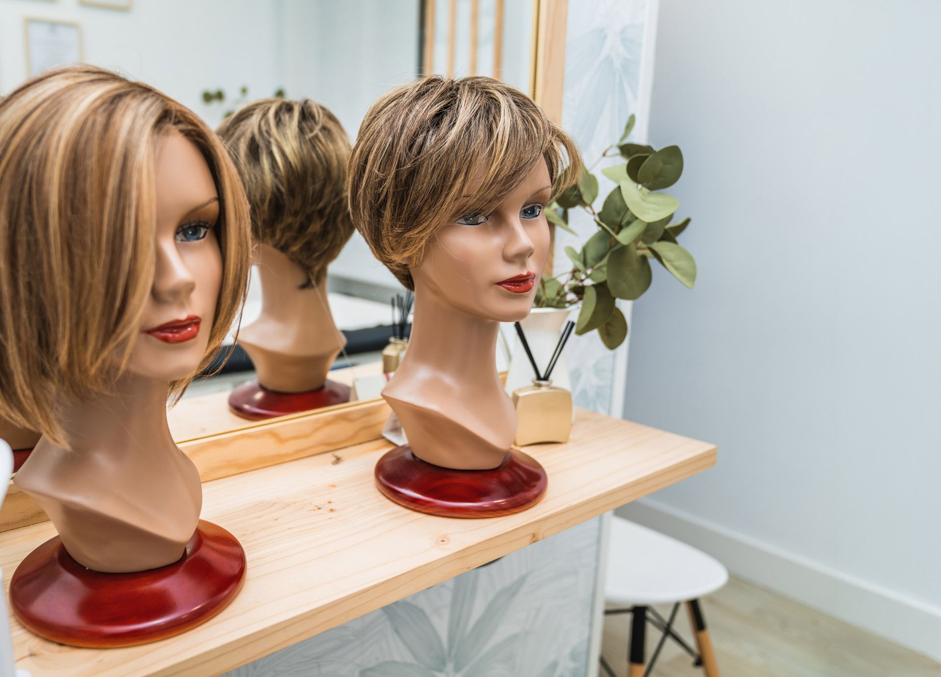 Three mannequin heads with wigs on them are sitting on a wooden table in front of a mirror.