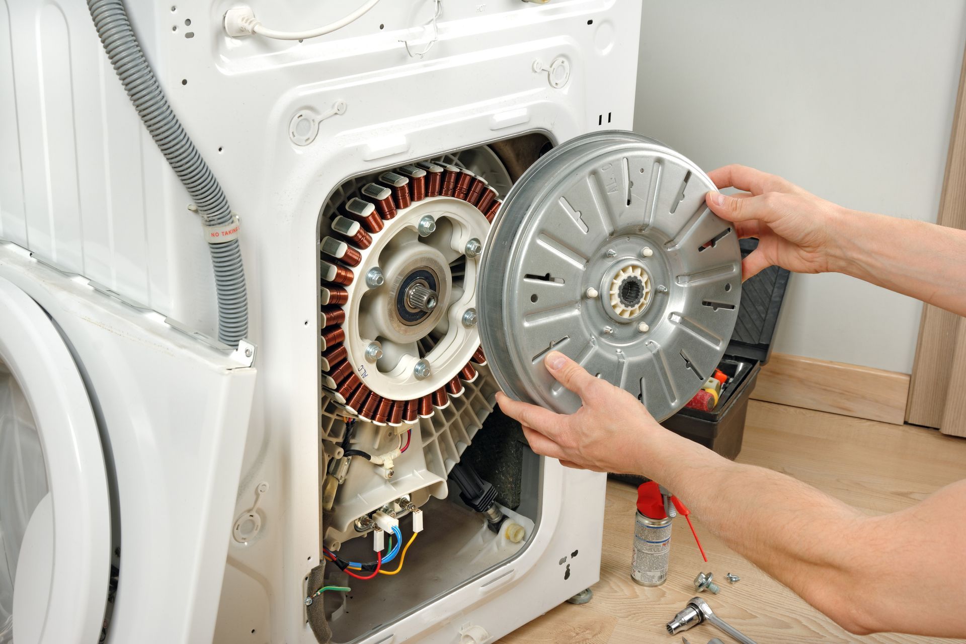 A person is repairing a washing machine by removing the motor.