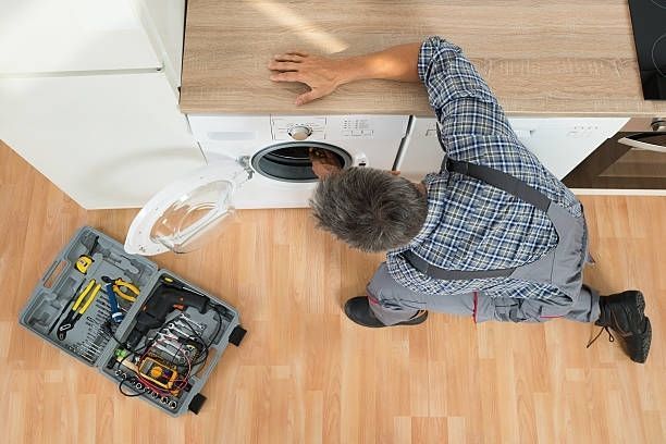 A man is fixing a washing machine in a kitchen.