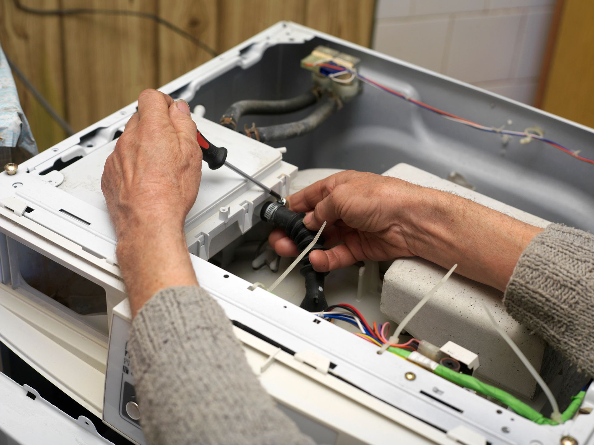 A person is fixing a washing machine with a screwdriver.