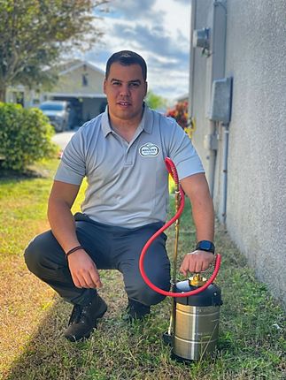 A man is kneeling down in the grass holding a sprayer.