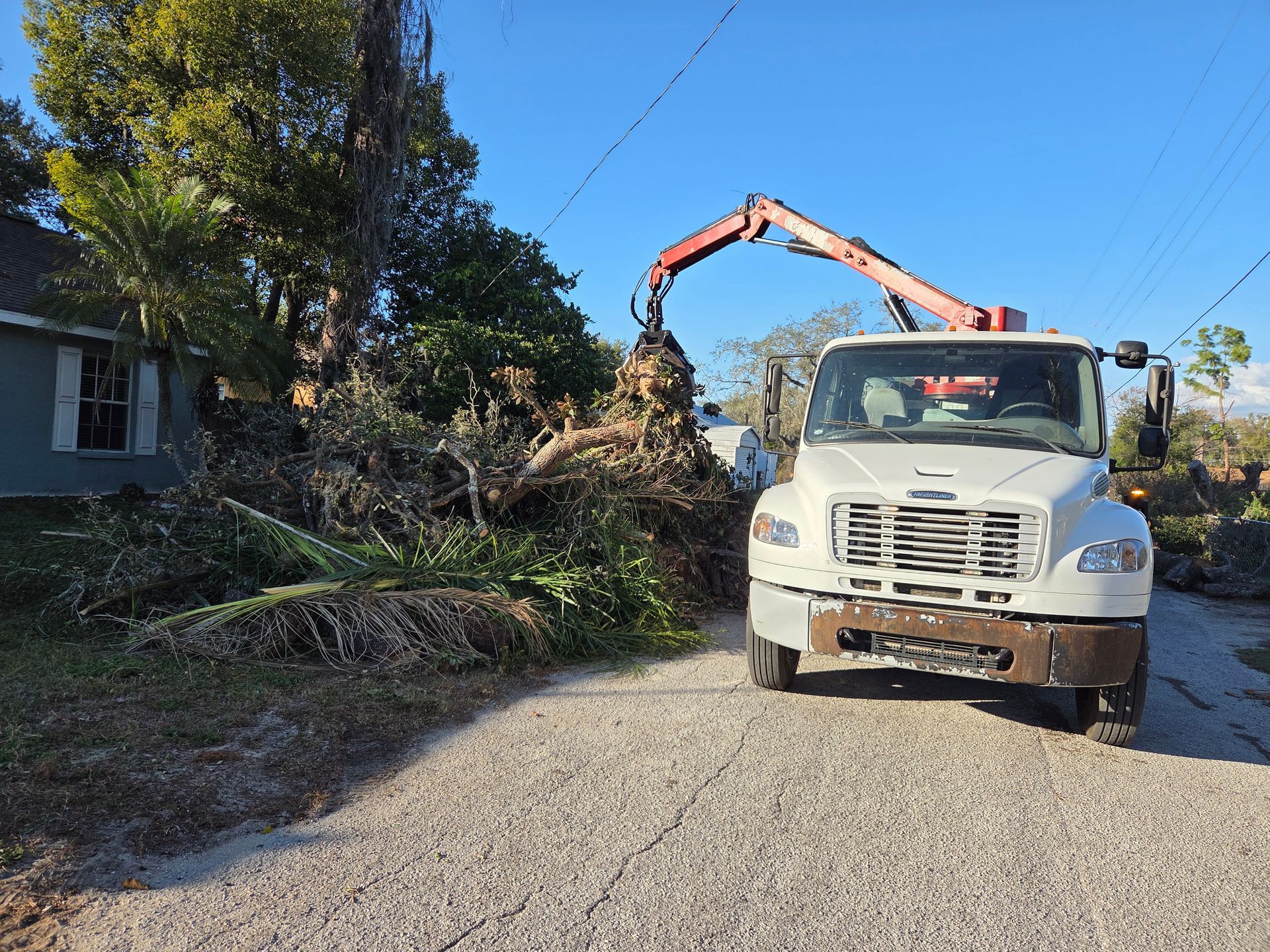 Grapple truck lifting tree debris near lowāhanging wires during a cleanup project in Plant City, Florida