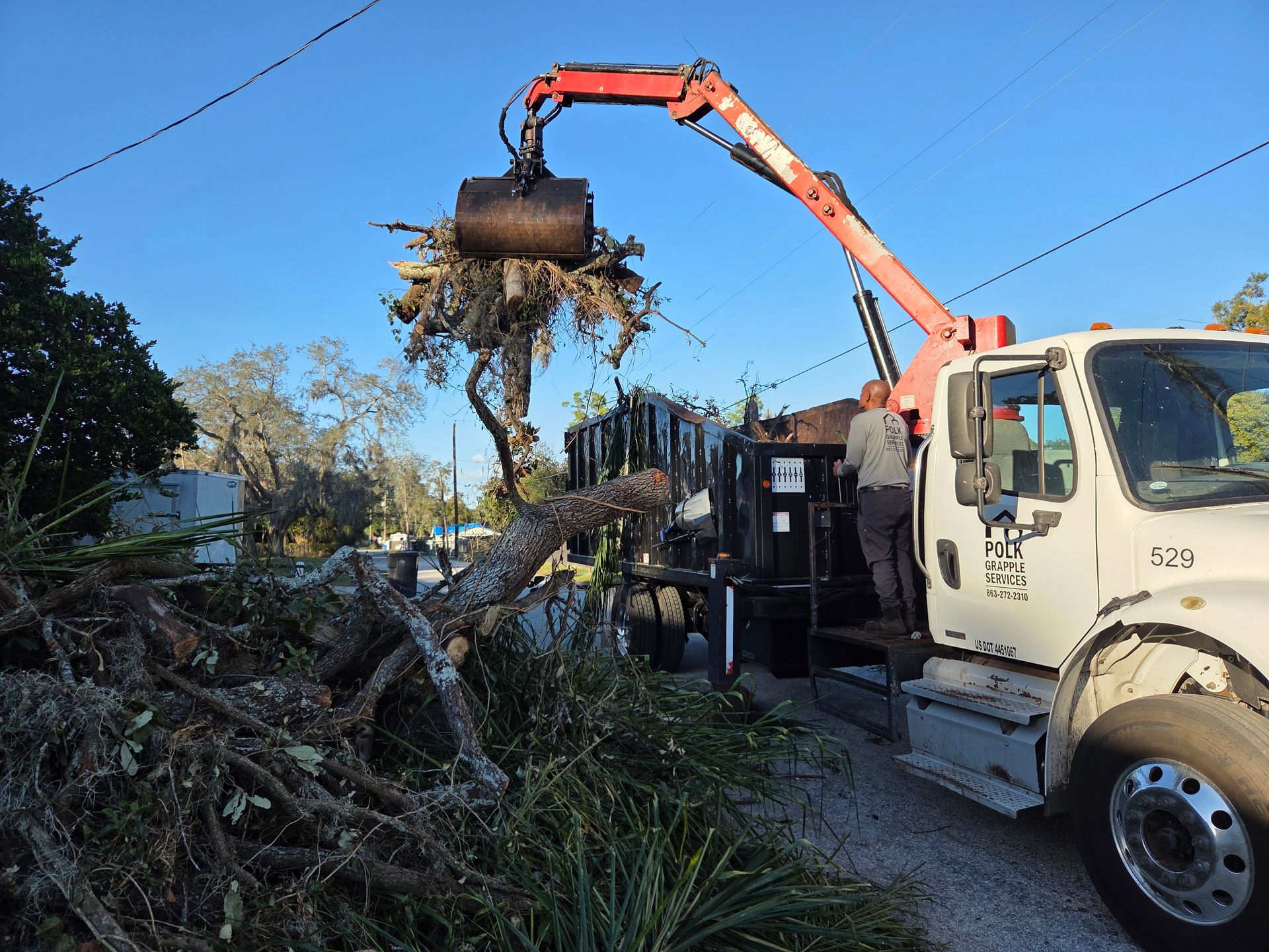 Grapple truck lifting and loading a large pile of tree debris during a cleanup project in Plant City, Florida