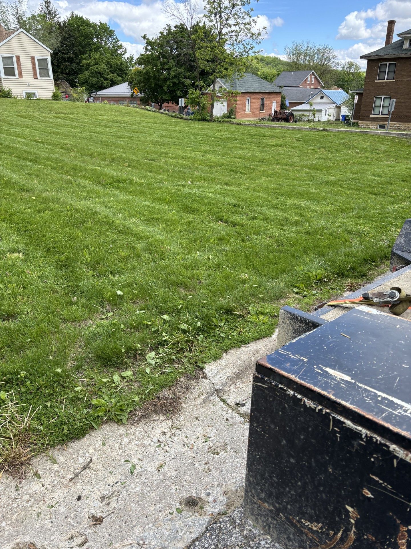 Person in blue overalls mowing a green lawn with a yellow and gray lawnmower on a sunny day.